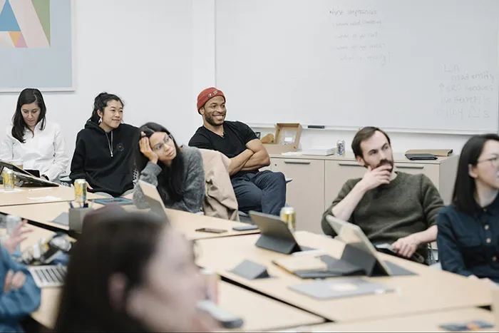Seven people sitting around a conference table all facing the camera; four women and two men on the right side are in focus and a woman on the left is out of focus.