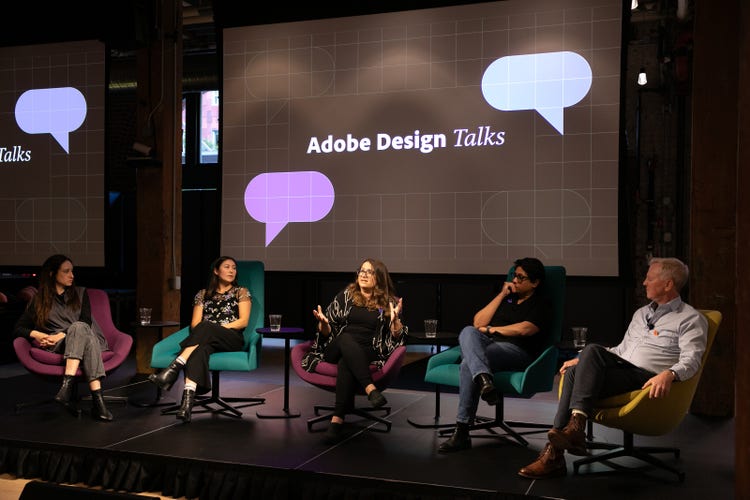 A photograph of four women and a man (far left) seated on a stage in front of a screen that reads Adobe Design Talks.