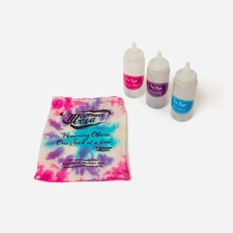 Three plastic squirt bottles (from left: with a pink label, purple label, and blue label), and a small drawstring bag tie-dyed—with the same pink, purple, and blue colors— are arranged on a table.