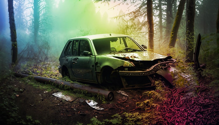 An AI-generated photograph of an abandoned, wrecked car (with a dented hood and front end) rotting into the earth in a fogged-in grove of trees overlaid with rainbow-hued, diagonal gradient.