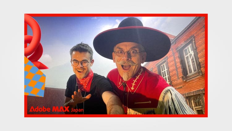 A photograph in a bold Adobe-red frame with the words Adobe MAX Japan in the lower left corner. In it, two men dressed in Western-themed clothes: on the left a young man with glasses is wearing a black shirt and a bright red bandana around the neck stands alongside a man wearing glasses, a wide-brimmed black hat, and a red western-shirt white fringe details with a bolo tie. Behind them, against a blue sky, is a rustic wooden building with large windows, suggesting an old Western-style town setting.