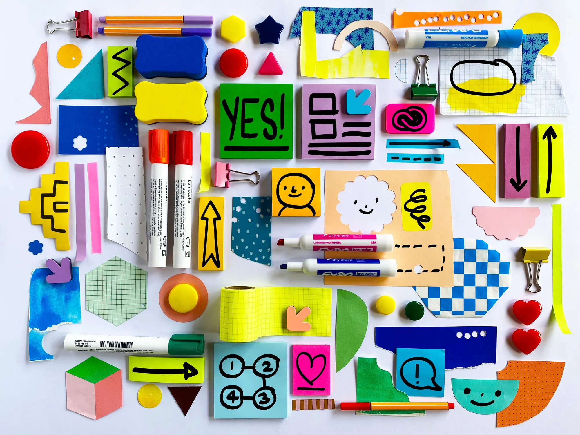 A colorful collection of writing tools and sticky notes, with drawn-on graphic art, arranged in an organized collage.